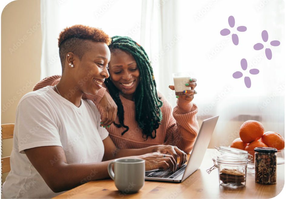 Two women drinking coffee while looking at a laptop.